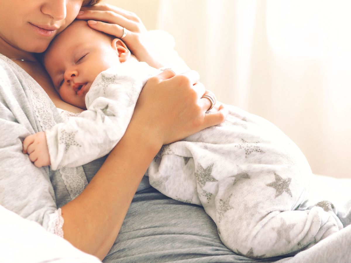 baby sleeping on mother's chest and mum's arms cradling the baby