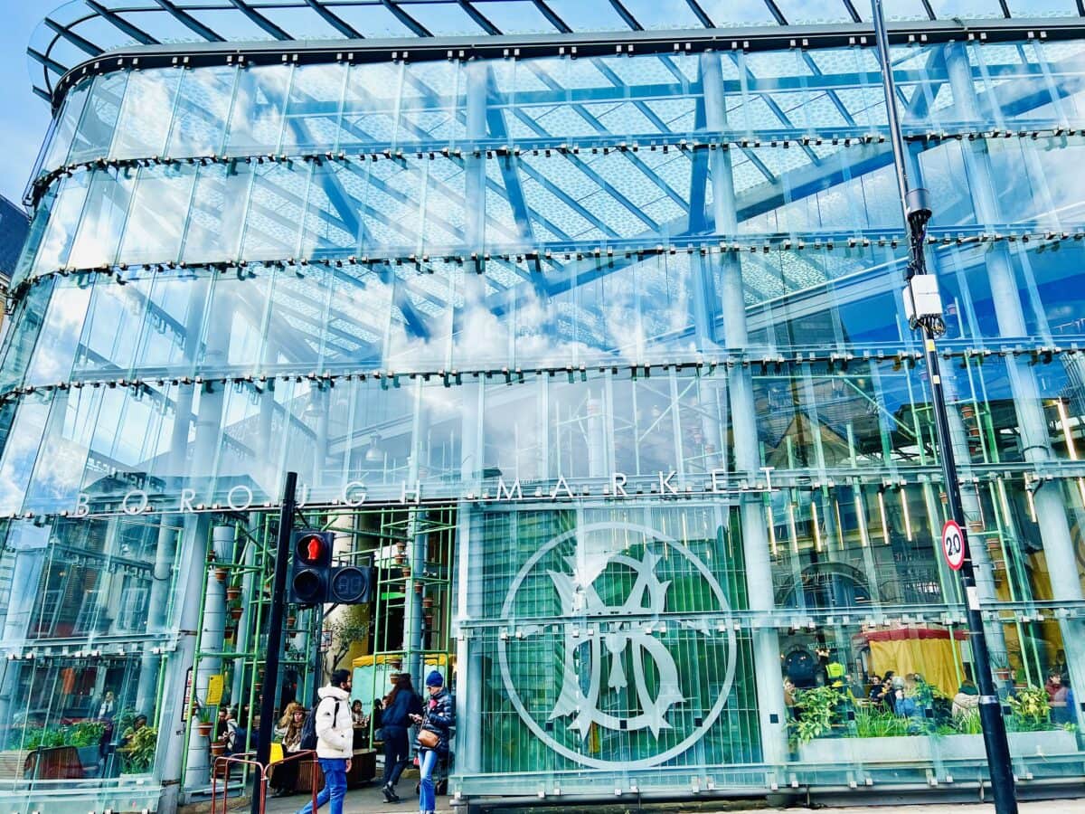 a shiny glass facade of Borough Market entrance which offers a seating area for customers near London Bridge Station