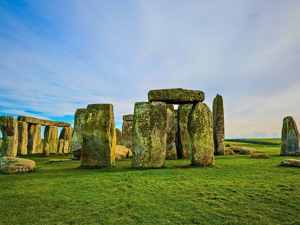 Side view of Stonehenge set against green grass and clear blue skies on Salisbury Plain.