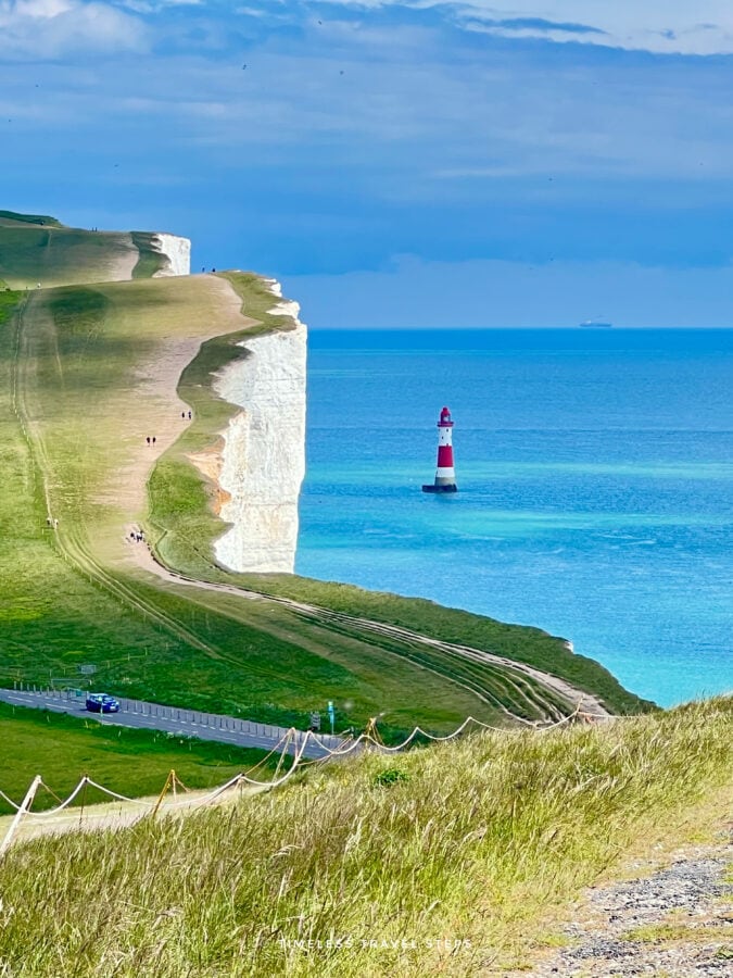 View of the red and white Beachy Head Lighthouse in the distance with turquoise sea and white chalk cliffs.
